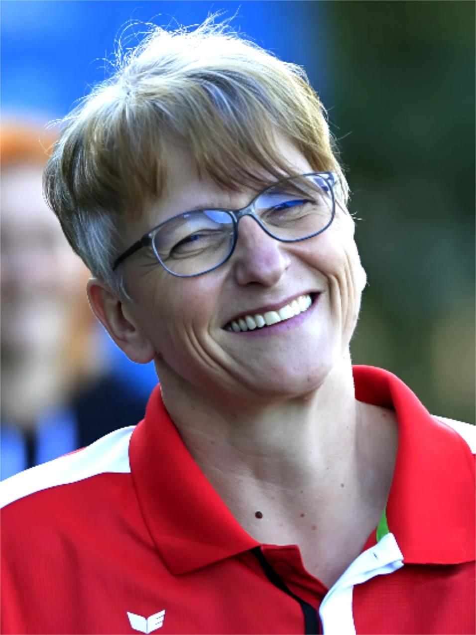 L&auml;chelnde Frau mit Brille in roter Sportbekleidung, Hintergrund unscharf.