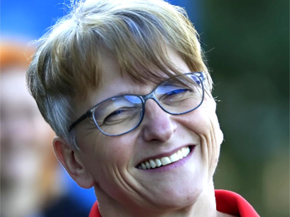 L&auml;chelnde Frau mit Brille in roter Sportbekleidung, Hintergrund unscharf.