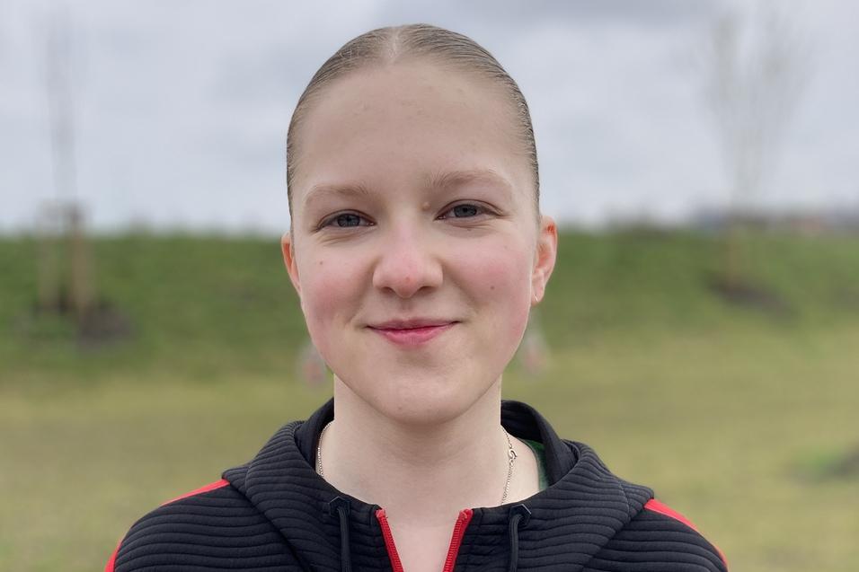 Luise Durdak Junge mit kurzen Haaren und rotem Sweatshirt steht lächelnd auf einem Sportplatz mit grünem Hintergrund.