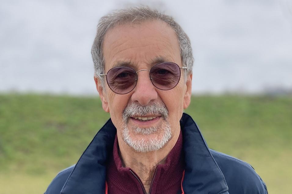 Hans-Ulrich Ruhnau Mann mit Brille und grauen Haaren steht vor einer Wiese mit Bäumen und bewölktem Himmel.
