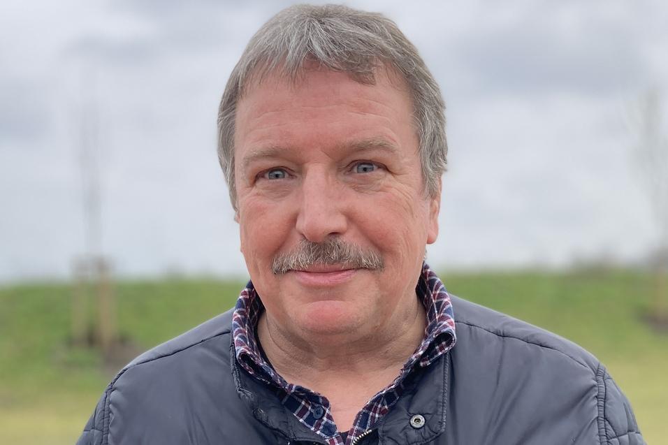 Holger Ewert Lächelnder Mann mit einem leicht grauen Haarschnitt, trägt eine schwarze Jacke und steht vor einer Wiese.