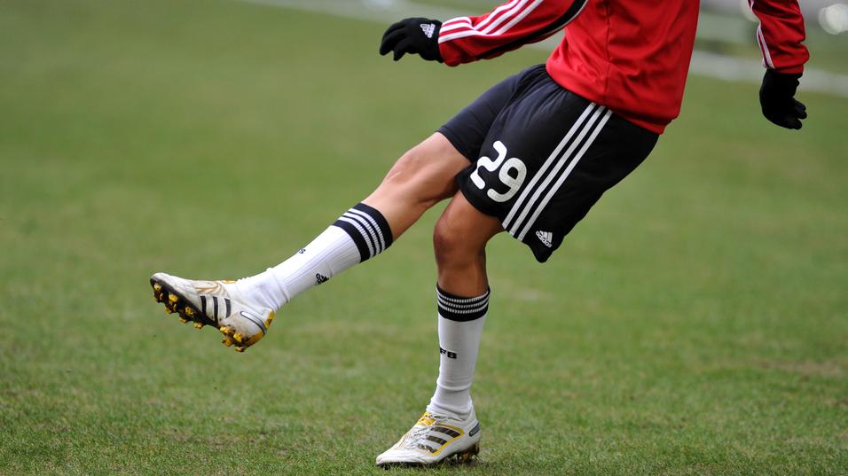 Nahaufnahme eines Fußballspielers mit einem roten Trikot, der auf einem Rasenfeld einen Ball mit dem rechten Fuß spielt.