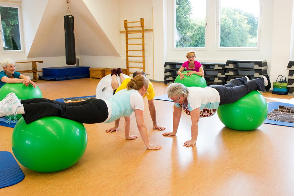 Gruppentraining auf Gymnastikbällen: Frauen führen Übungen in einem hellen Raum mit Holzboden und weißen Wänden aus.